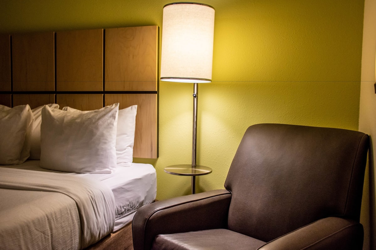 A hotel room with a bed, a brown leather chair, and a floor lamp.