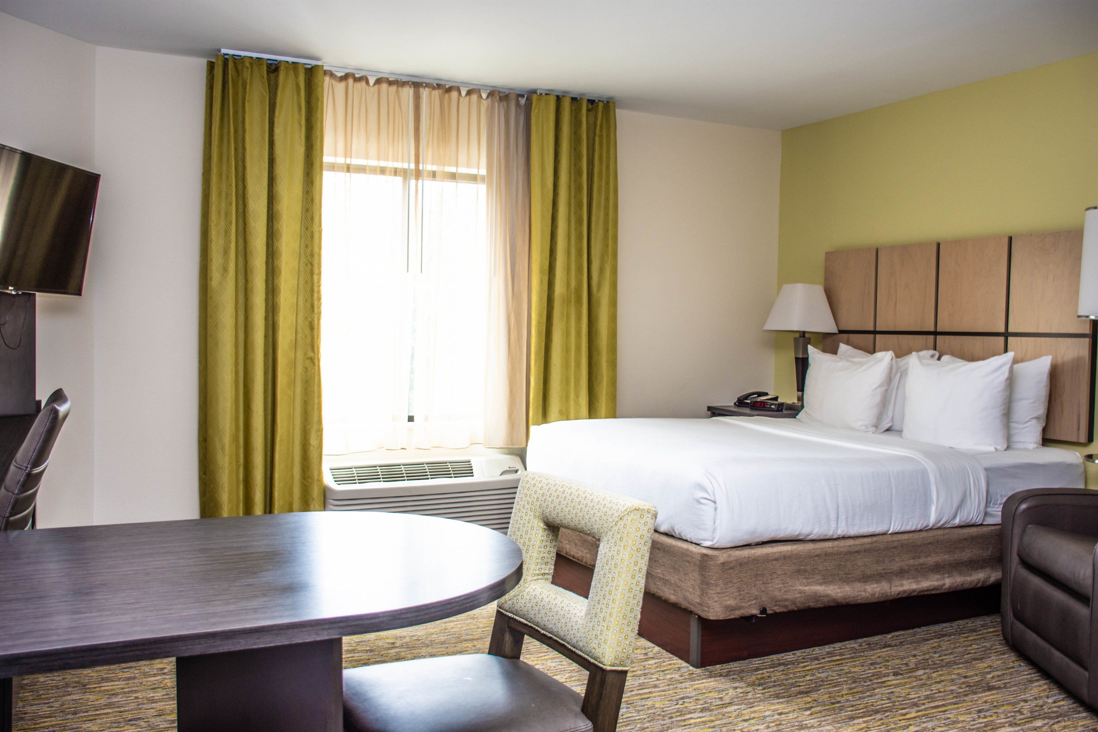 A hotel room with a bed, a desk, a chair, a TV, and a window with curtains.