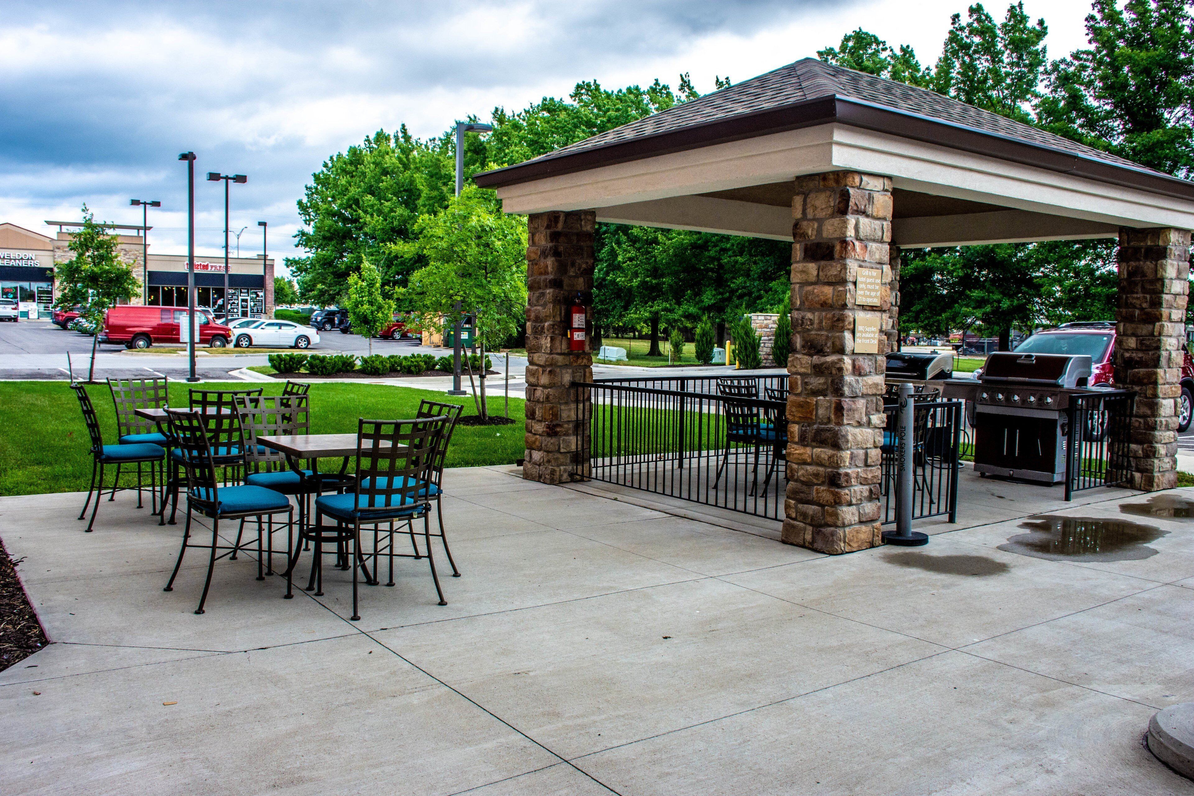An outdoor patio with stone pillars, a covered seating area, and a grill.