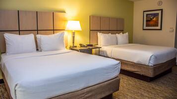 A hotel room with two beds, a nightstand, a lamp, a clock, and a framed picture on the wall.