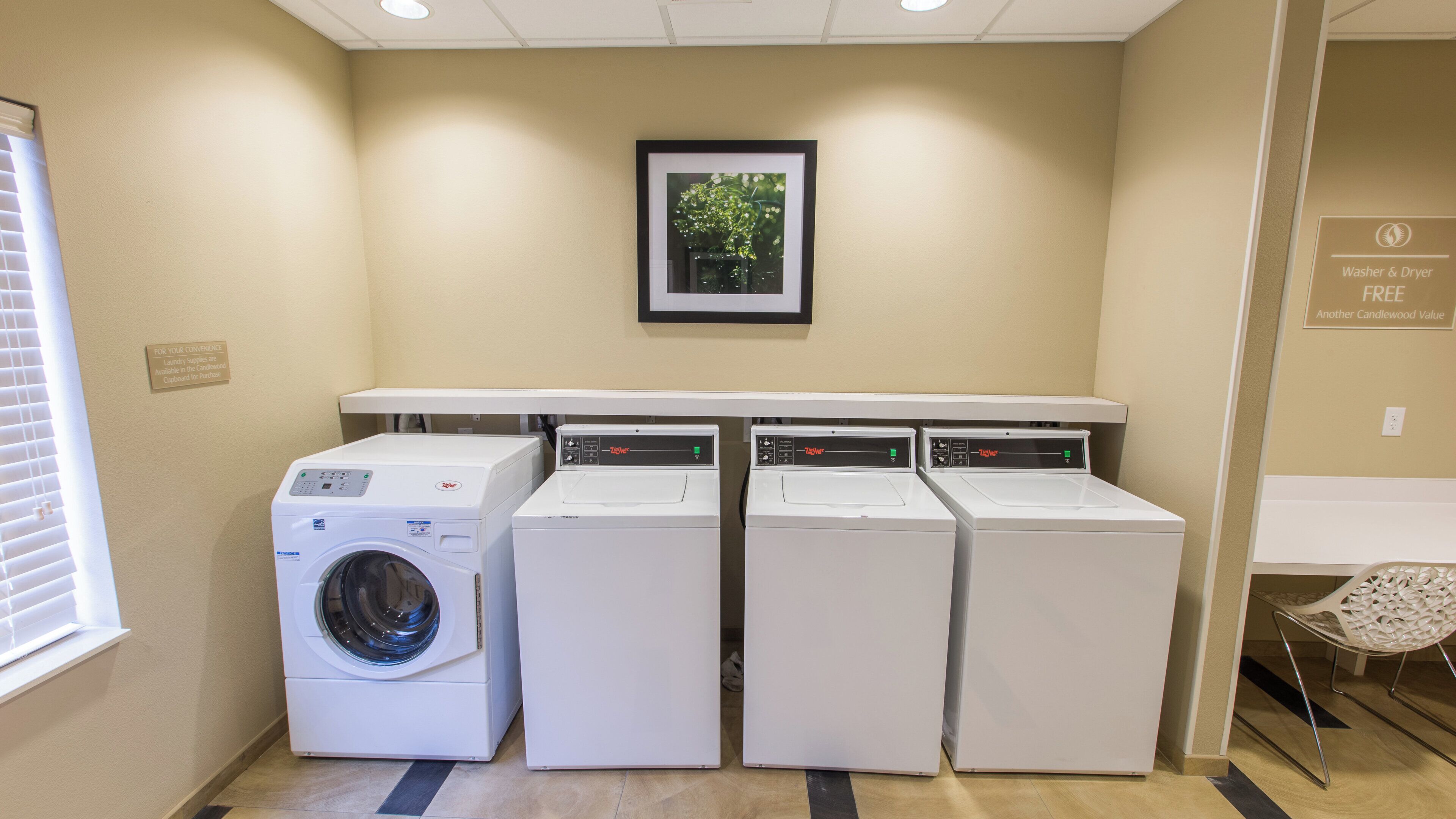 A laundry area with four washers and dryers, a framed picture on the wall, and a sign indicating free washer and dryer use.