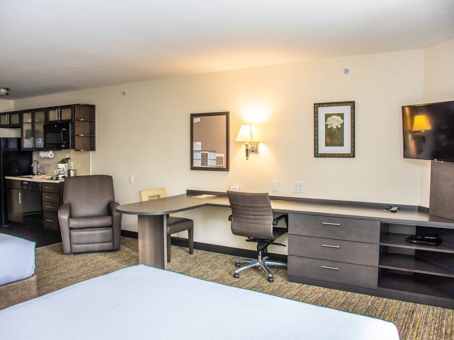 A hotel room with a bed, a desk, a chair, a television, a microwave, and a refrigerator.