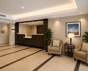 A hotel lobby with a reception desk, two armchairs, a lamp, and a framed picture on the wall. - Candlewood Suites San Antonio Airport by IHG (San Antonio)
