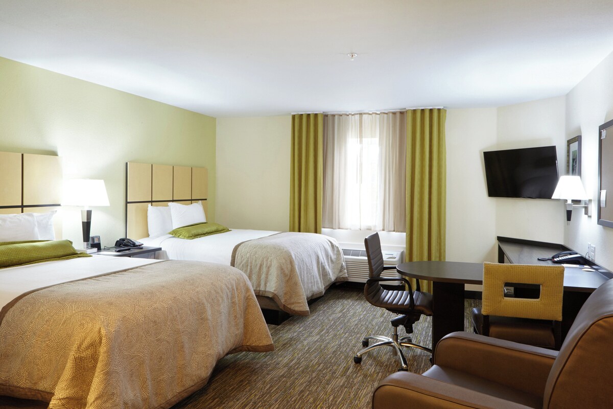A hotel room with two beds, a desk, a chair, a television, and a window with curtains.
