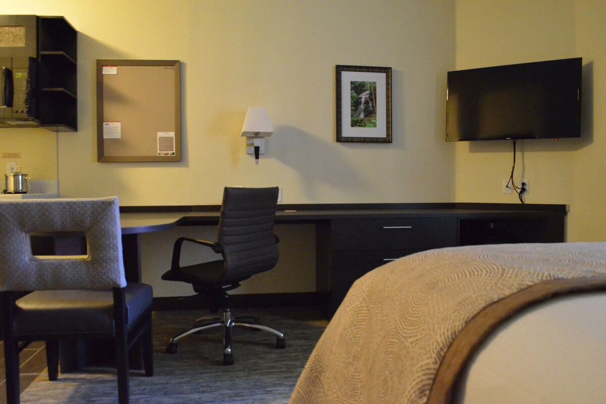 A hotel room with a bed, a desk, a chair, a television, and a wall-mounted light.