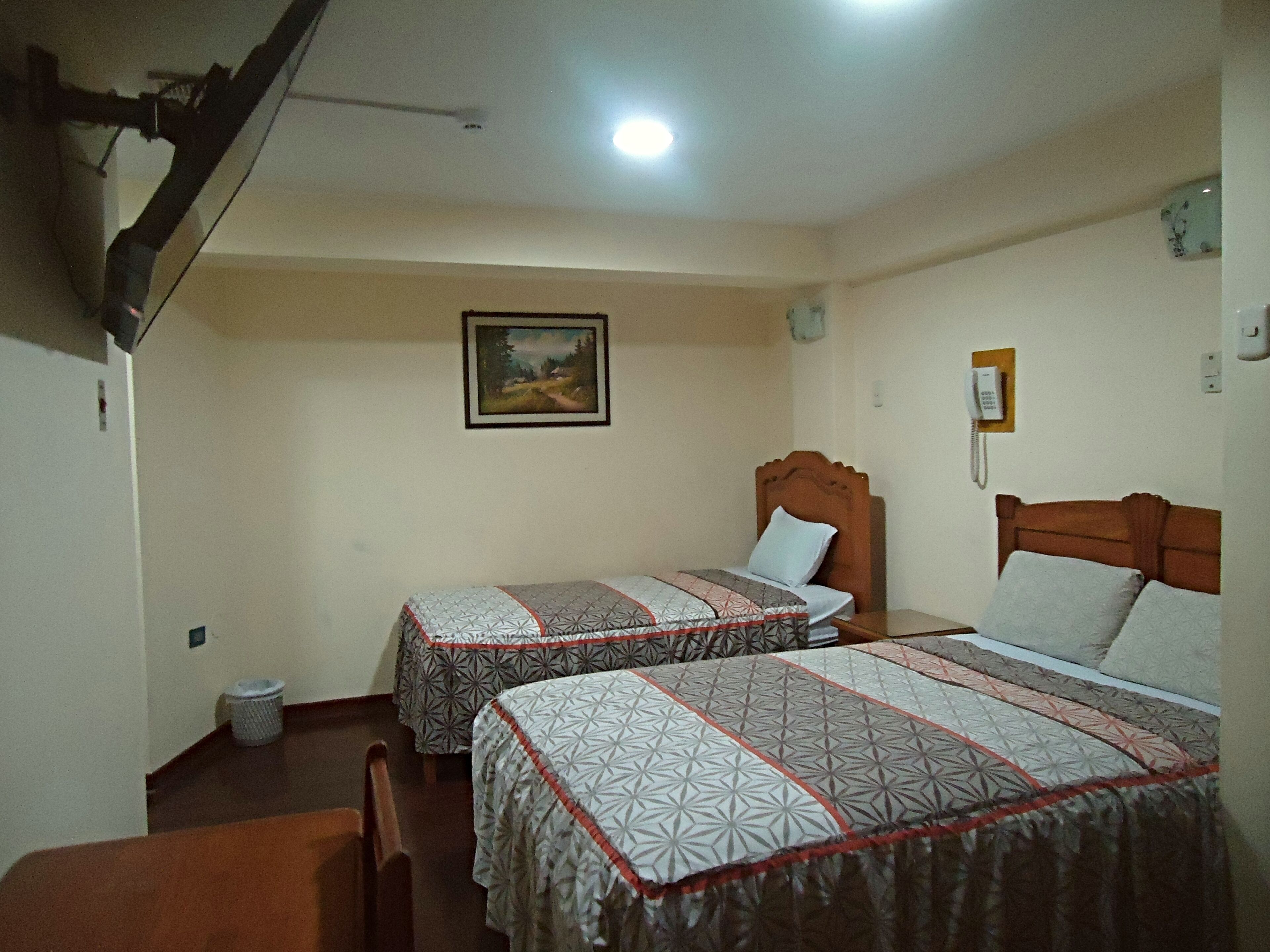 Habitación de hotel con dos camas, un cuadro en la pared, un teléfono y un cesto de basura.