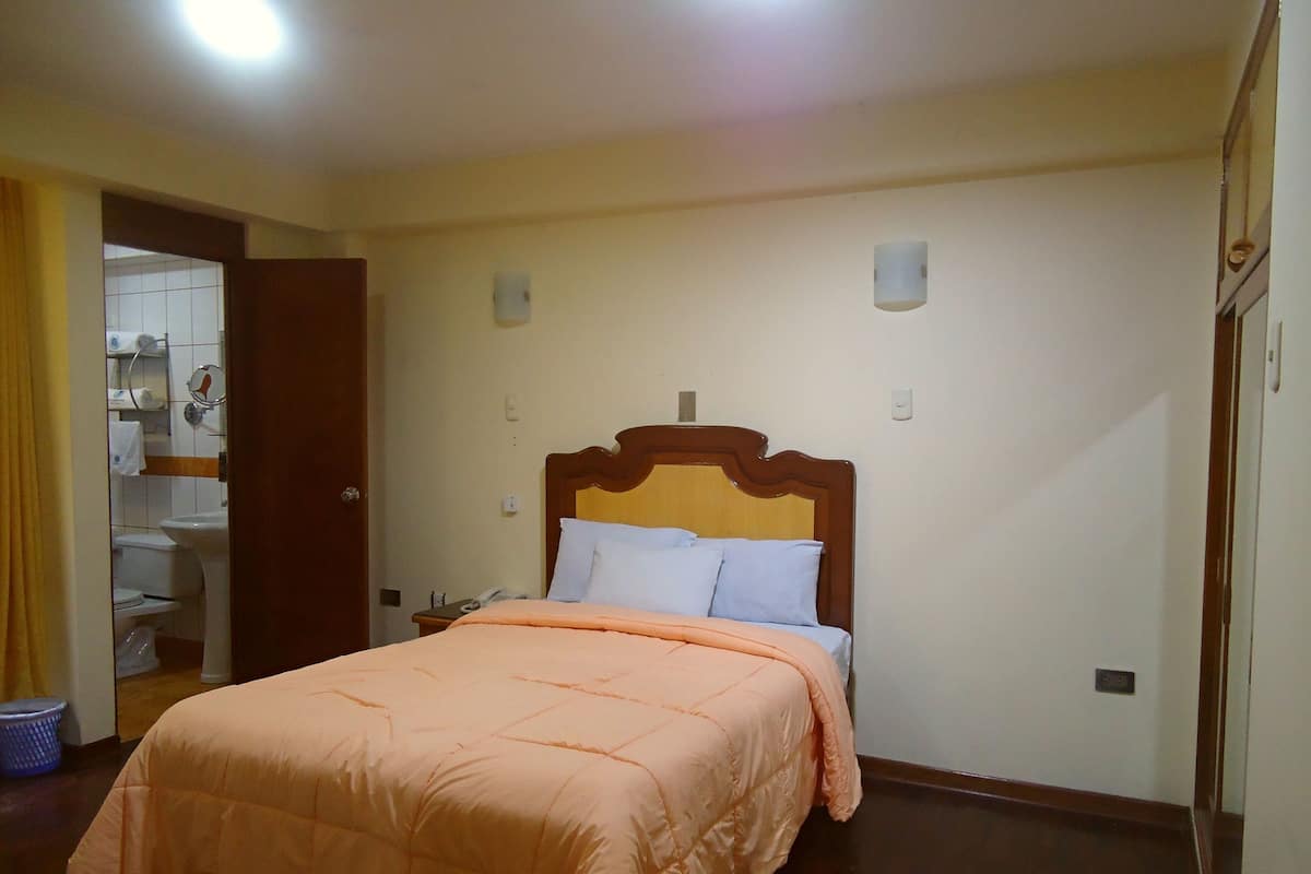 A bedroom with a bed, a wooden headboard, a nightstand, and a bathroom visible through an open door.