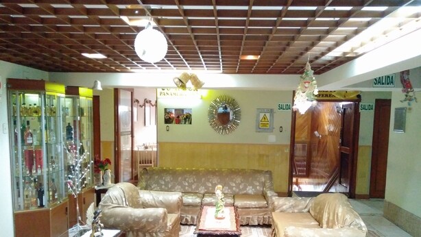 A lobby with a sofa, chairs, a glass cabinet with bottles, a mirror, and a ceiling with wooden beams. - Hotel Panamericano (Lima)
