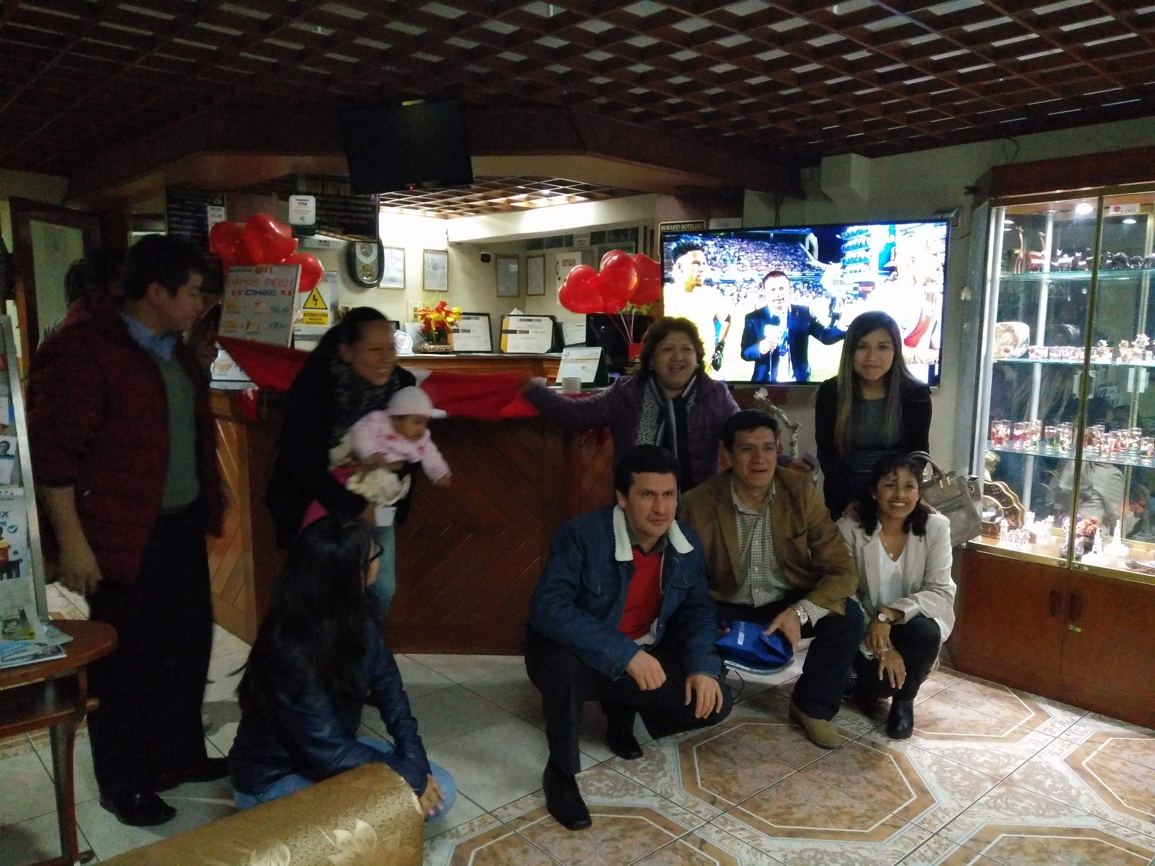 Un grupo de personas en una sala con una mesa de recepción, un televisor y una vitrina de vidrio con objetos.