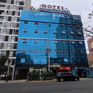 Ein modernes Hotelgebäude mit einer glänzenden Glasfassade, einem gut sichtbaren Schild mit der Aufschrift 'HOTEL PANAMERICANO' und einem einladenden Eingang.