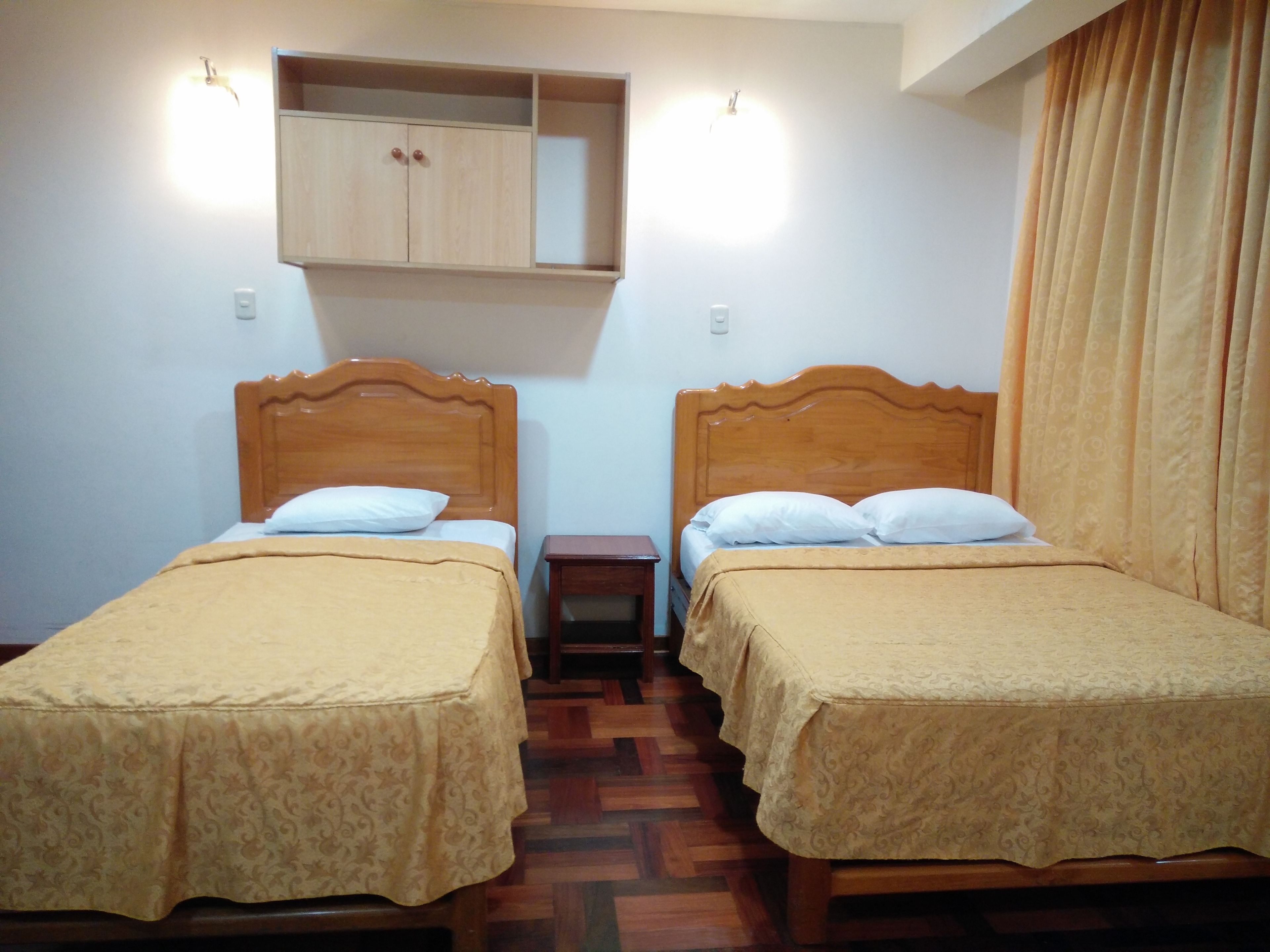 Una habitación con dos camas de madera, cada una con cabecero, mesita de noche y estante sobre las camas.