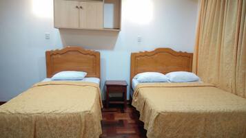Una habitación con dos camas de madera, cada una con cabecero, mesita de noche y estante sobre las camas.