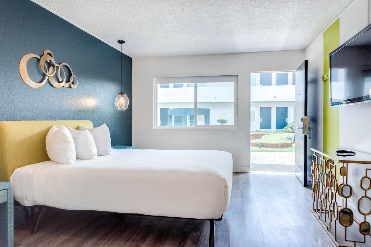 Ett modernt hotellrum med en stor säng, utsikt över byggnadens fasad och en tv på väggen.