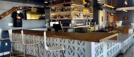 A bar area with a wooden counter, bar stools, and shelves stocked with bottles.
