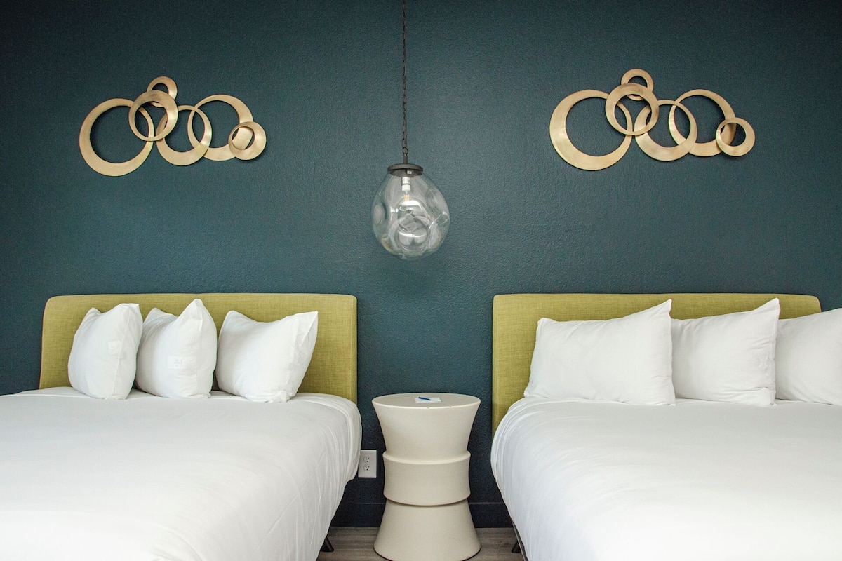 Ett hotellrum med två sängar, en väggmonterad lampa och dekorativ väggkonst.