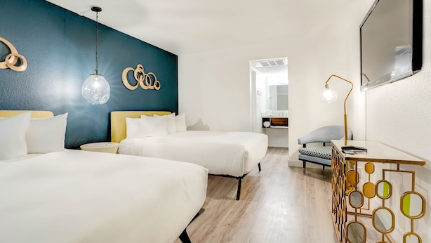 Een hotelkamer met twee bedden, een bureau, een stoel, een grote spiegel en een decoratieve muur met geometrische patronen.