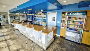Een bar met witte stoelen, een houten toonbank en een automaat met de tekst 'Goodies'.