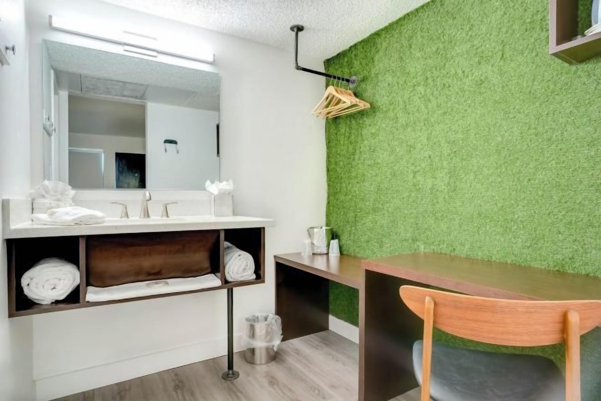 A modern bathroom with a green wall, a wooden chair, and a mirror above the sink.