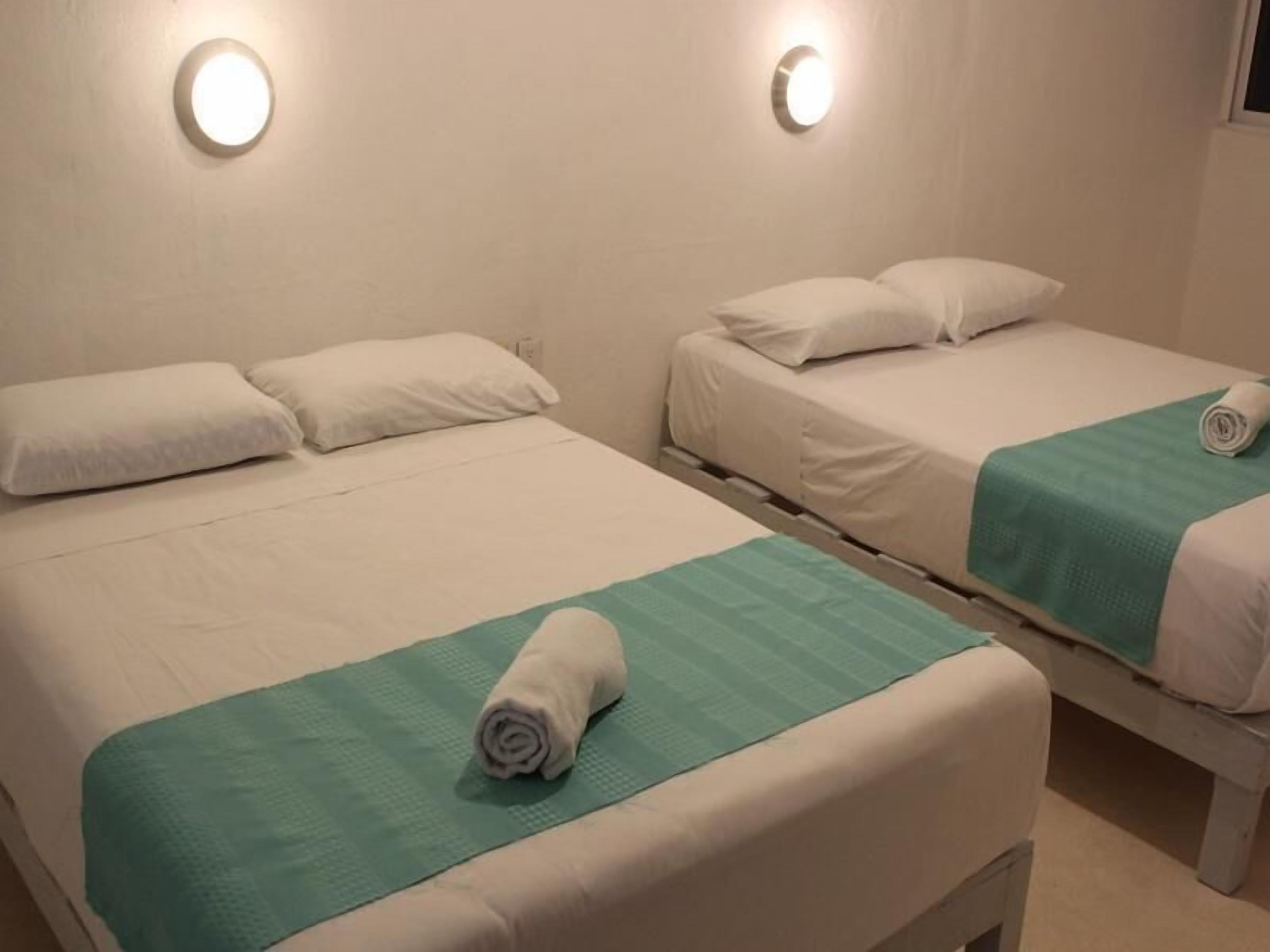 Two single beds with white linens, green bedspreads, and round wall sconces.