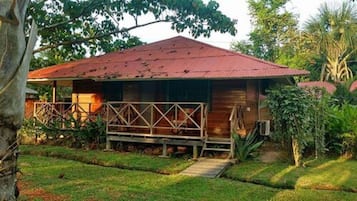 Una cabaña de madera con techo rojo, rodeada de abundante vegetación y árboles.