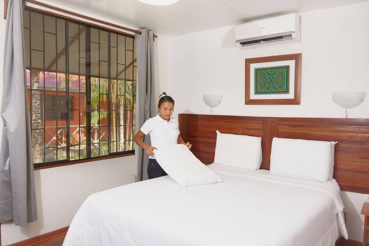 Ein Hotelzimmer mit Bett, einem vergitterten Fenster, einer Wandklimaanlage und einem gerahmten Kunstwerk.