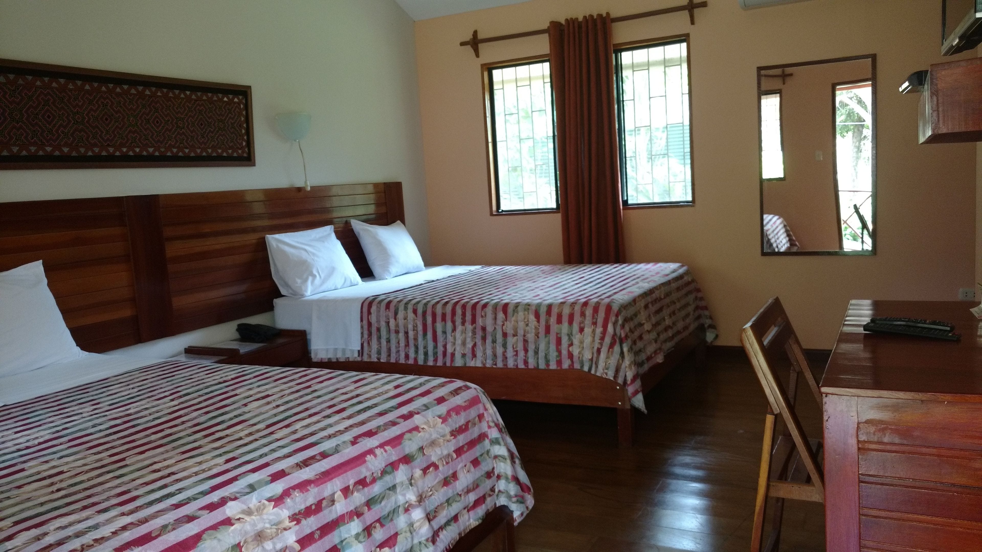 Een hotelkamer met twee bedden, houten hoofdborden, een bureau en een stoel.