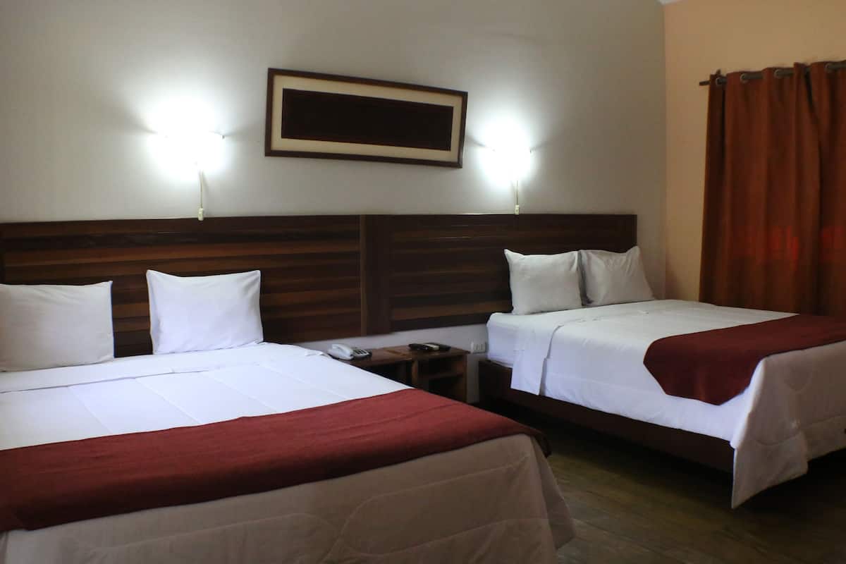Ein Hotelzimmer mit zwei Betten, einem Holzkopfteil, einem Nachttisch mit Telefon und Fernbedienung sowie einem gerahmten Bild an der Wand.
