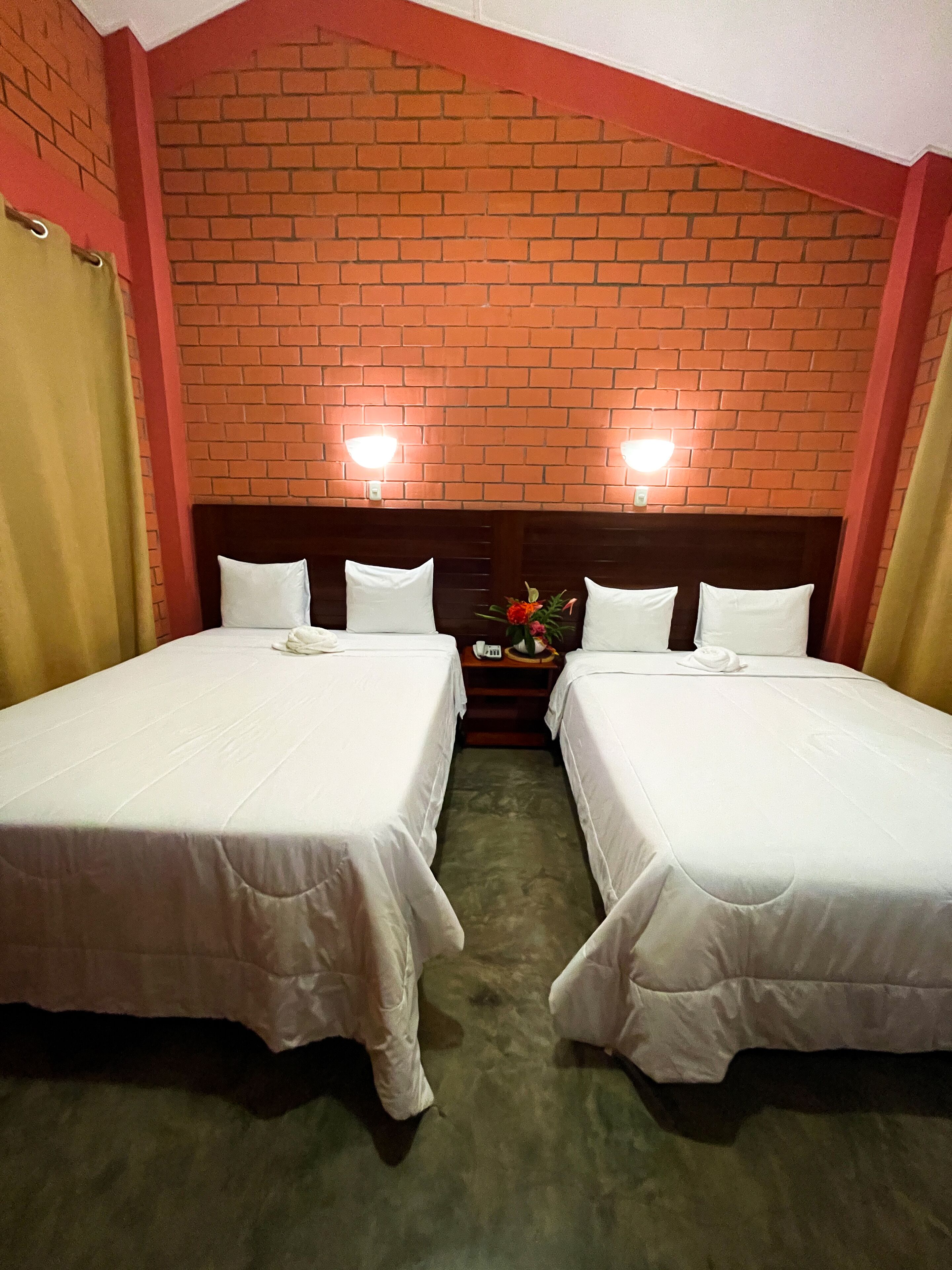 Habitación de hotel con dos camas individuales, una pared de ladrillo y dos luces fijadas a la pared.