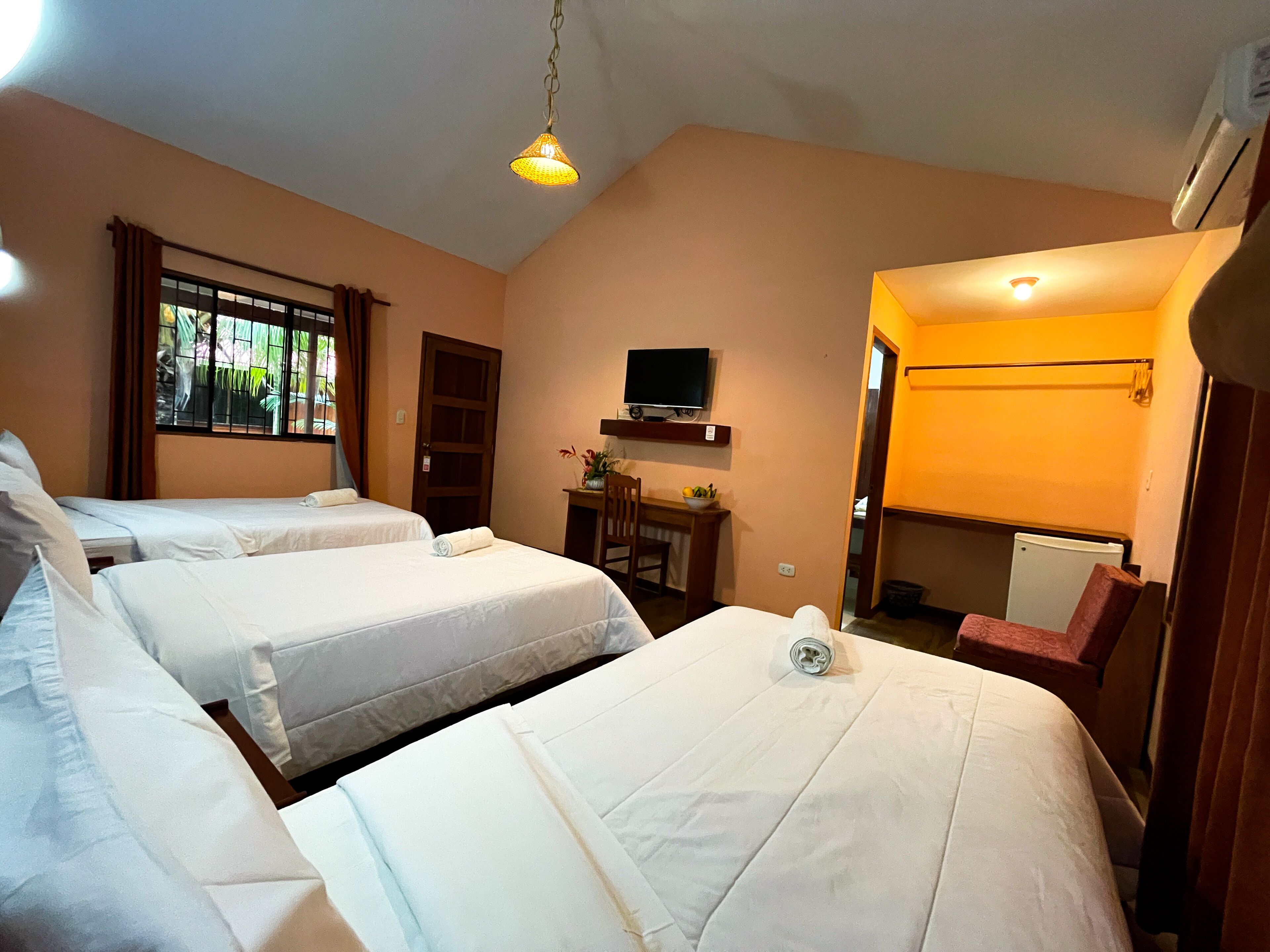 Habitación de hotel con dos camas, un escritorio, una silla, un televisor y una ventana con cortinas.