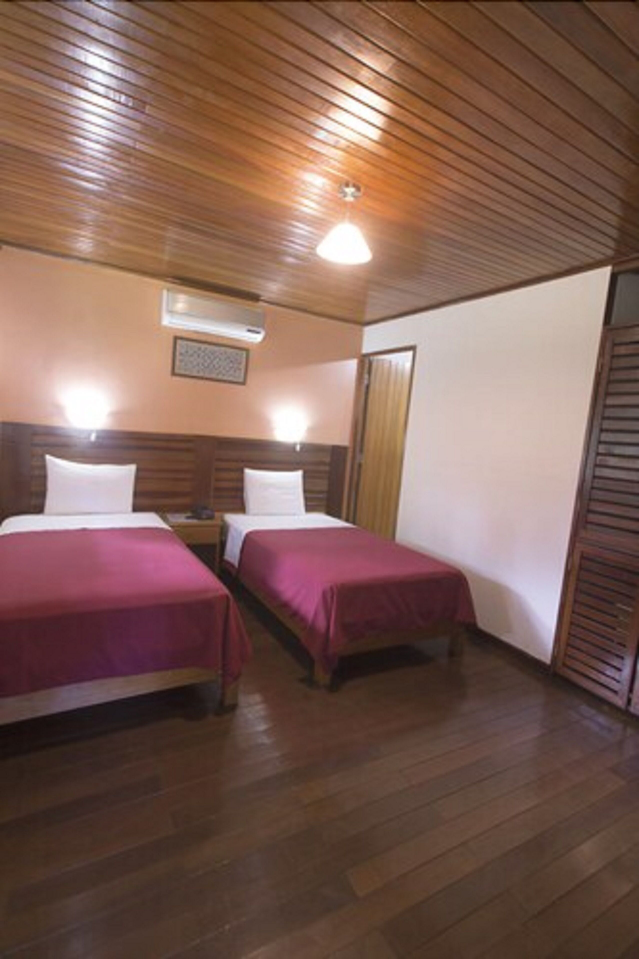 A room with two beds, wooden flooring, a ceiling fan, and a wall-mounted air conditioner.