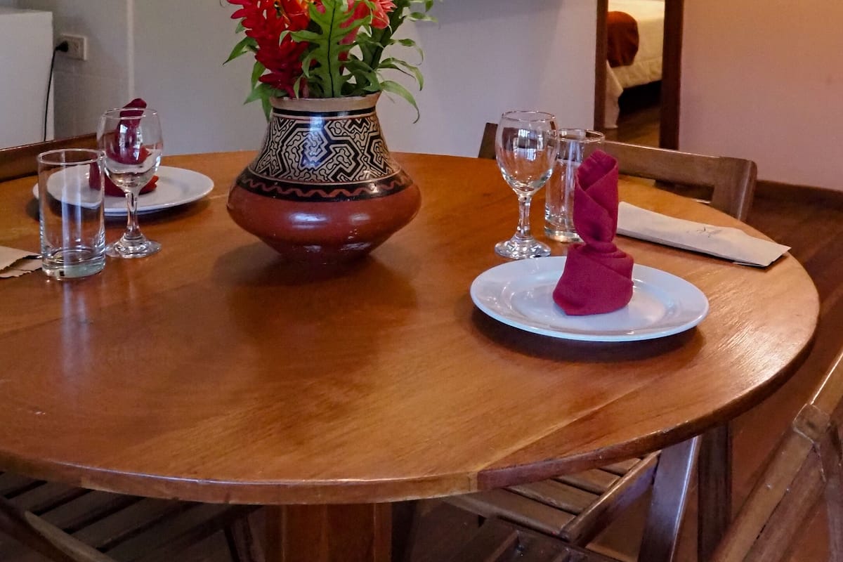 Ein Essbereich mit Holztisch, Stühlen, einer Vase mit Blumen und einem an der Wand befestigten Fernseher.