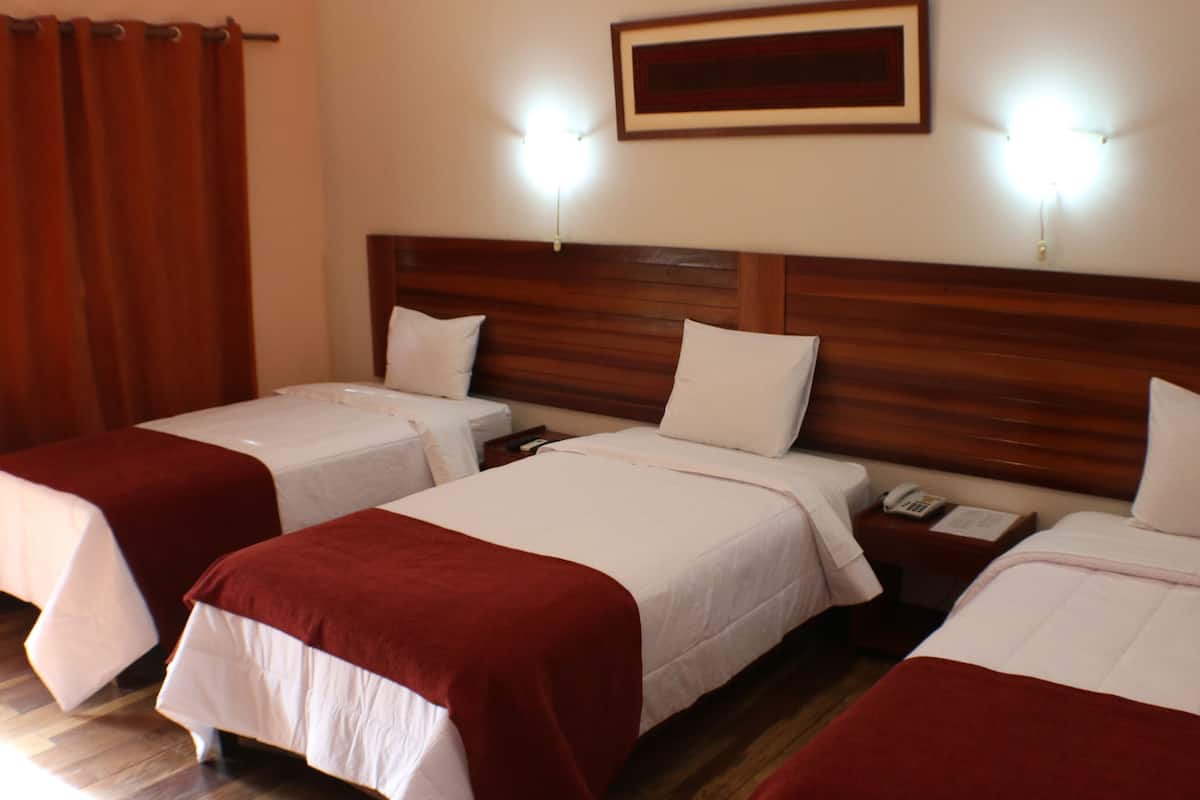 Ein Hotelzimmer mit drei Betten, jedes mit weißer Bettwäsche und roten Kopfteilen. Über den Betten befinden sich zwei Wandlampen und an der Wand ein gerahmtes Bild.