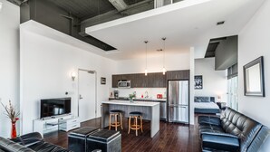 A modern living space with a kitchen, a dining area, and a seating area with a sofa and ottoman.