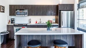 A modern kitchen with dark wood cabinets, stainless steel appliances, a central island with stools, and a large window providing natural light.