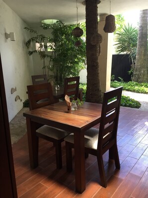 Una mesa de comedor de madera con cuatro sillas, rodeada de plantas en macetas y cestas colgantes.