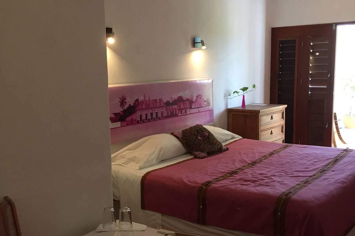 Un dormitorio con cama, mesita de noche, mesa de madera, ventilador de techo y luz en la pared.