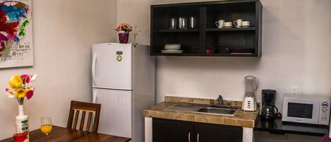 A compact kitchen with a refrigerator, a coffee maker, a microwave, and a sink.
