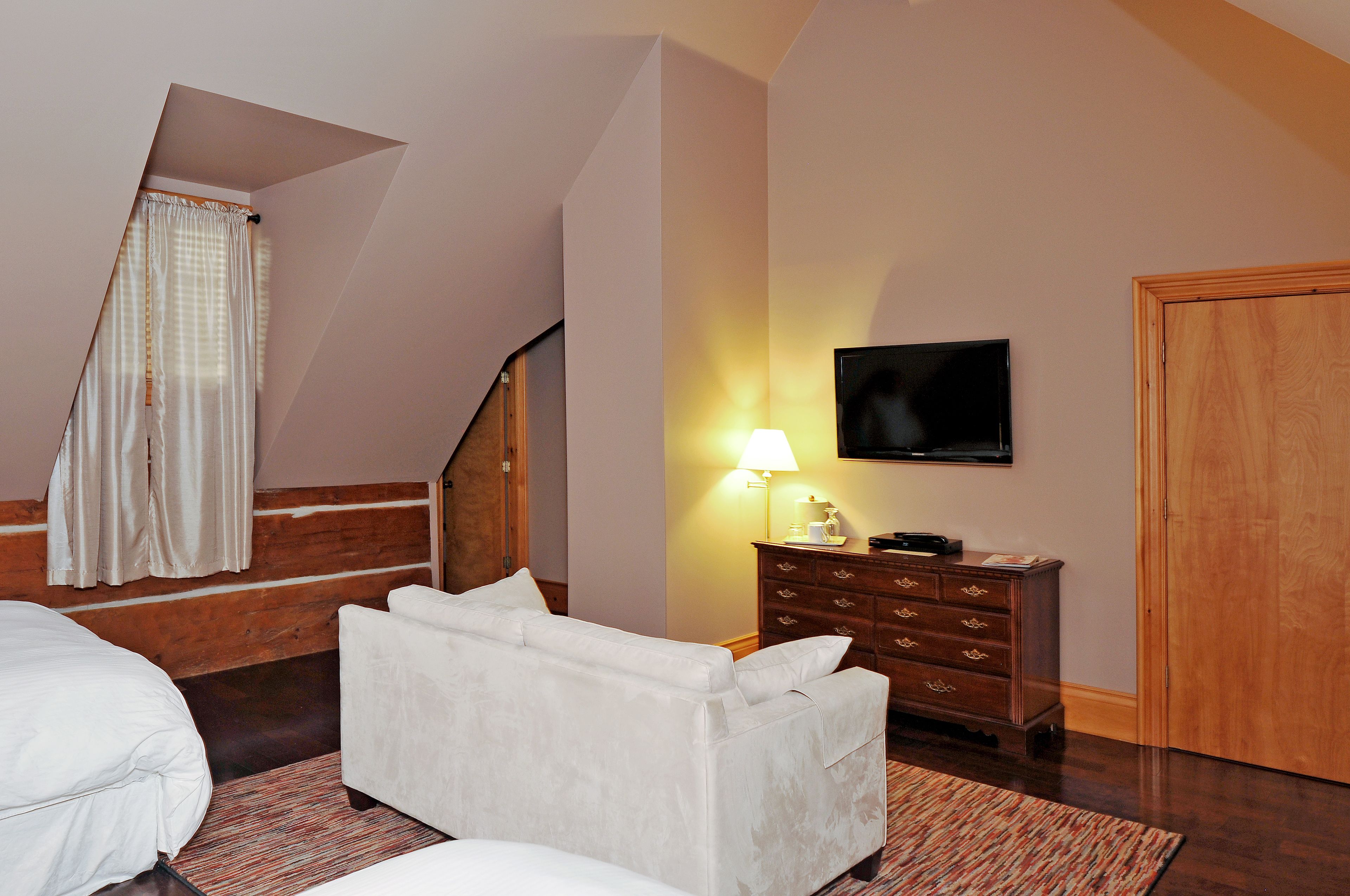 Un dormitorio con cama, sofá, cómoda, televisor y escalera.