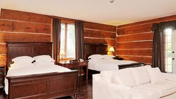 A log cabin-style room with two beds, a white sofa, wooden walls, and a window with curtains.