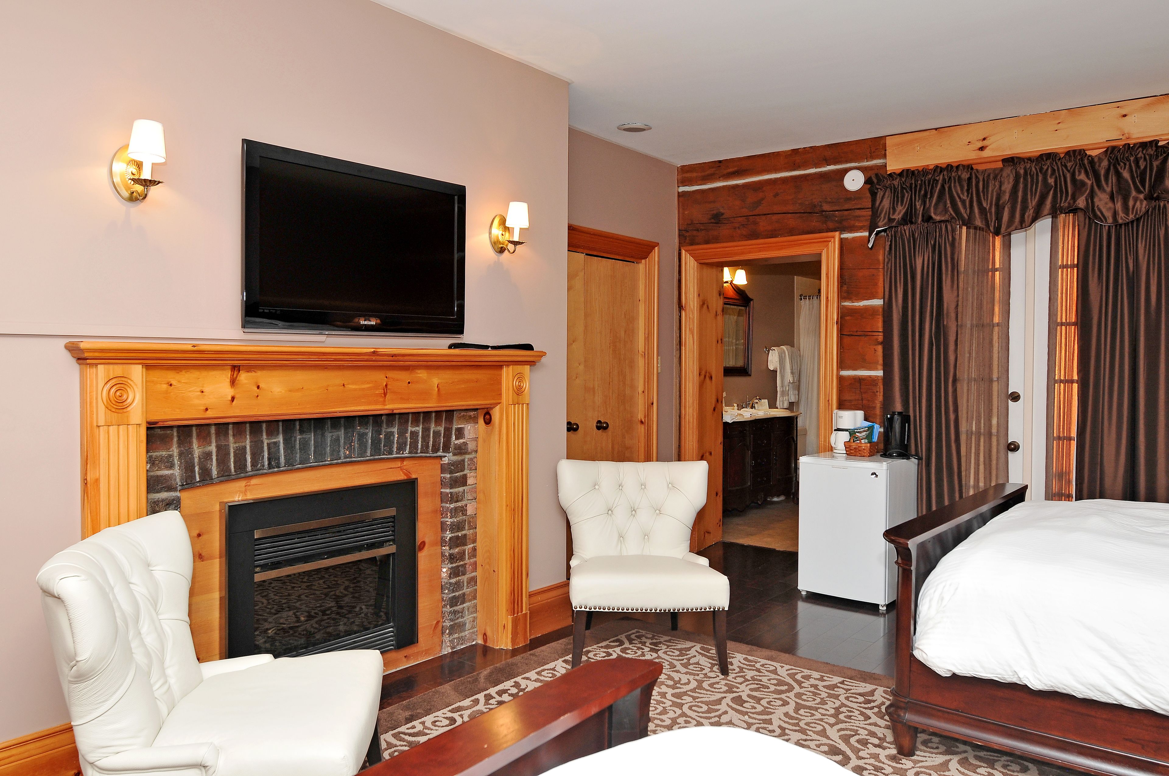 A hotel room with a fireplace, a television, a bed, a chair, and a desk.