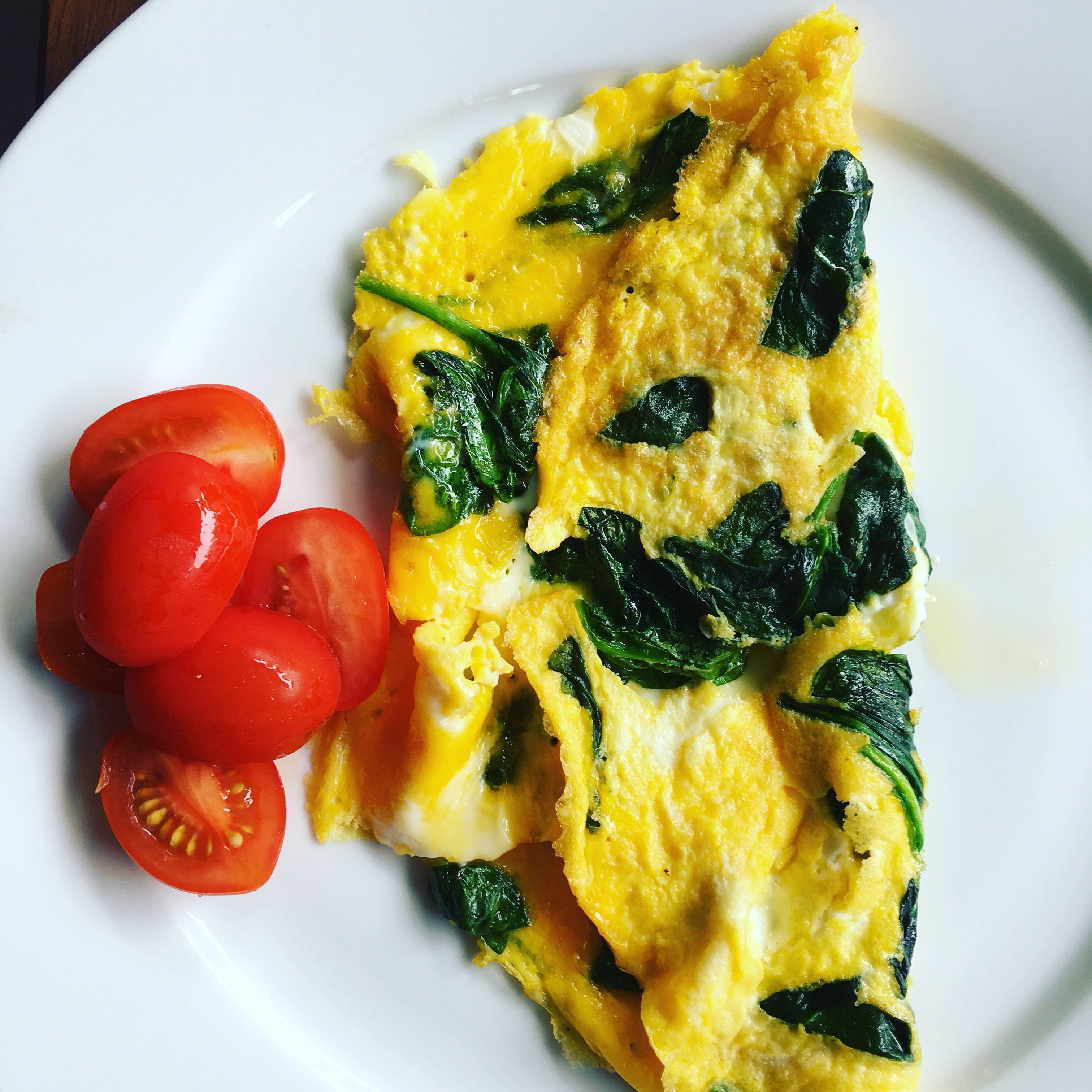 Un plato con una tortilla, espinacas y tomates en rodajas.