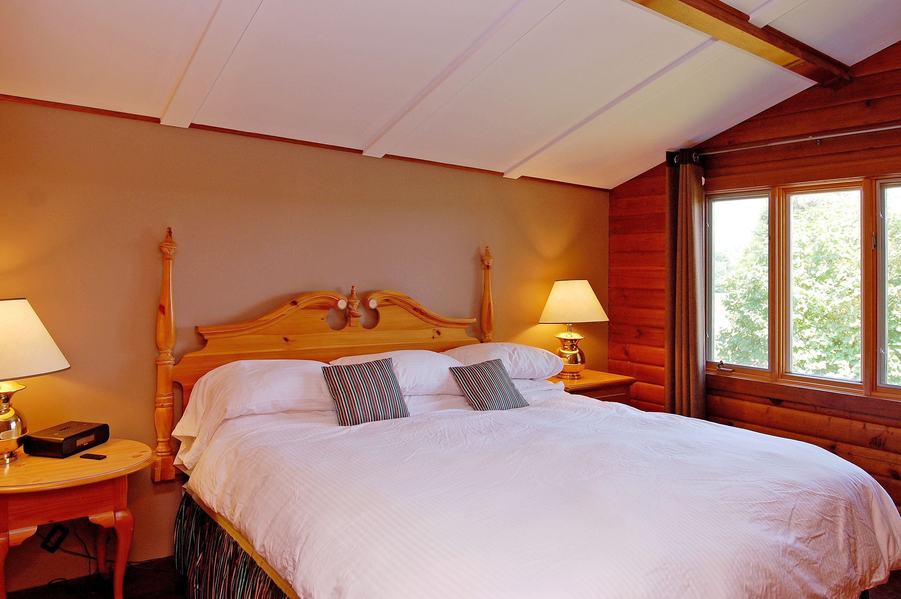 A neatly made bed with white linens and two striped pillows, wooden headboard, and two bedside lamps on wooden nightstands.