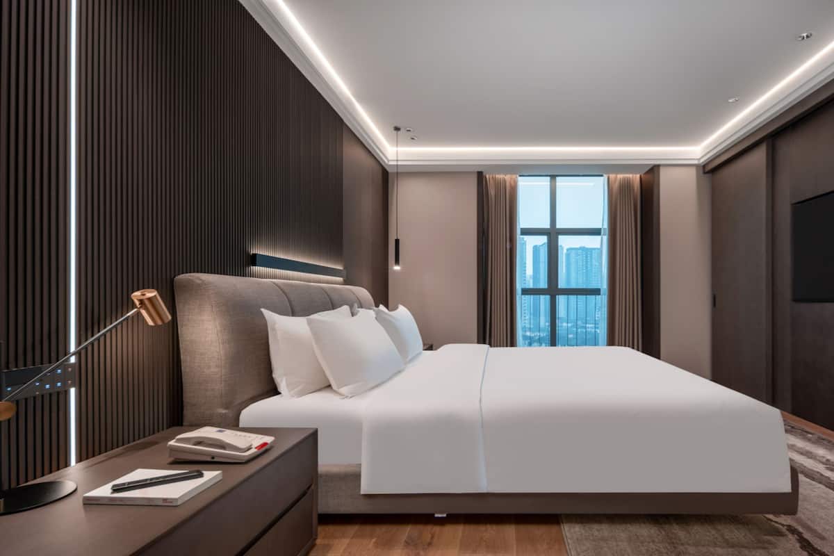 Habitación de hotel moderna con una cama grande, una mesita de noche con lámpara, un televisor de pantalla plana y vistas a la ciudad a través de la ventana.