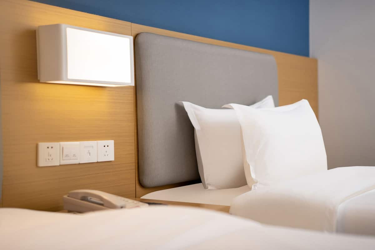 Habitación de hotel con cama, teléfono en la mesita de noche, luz empotrada en la pared y enchufes.