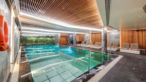 Una piscina interior moderna amb terra de vidre, sostre de fusta i zona de relaxació amb seients.