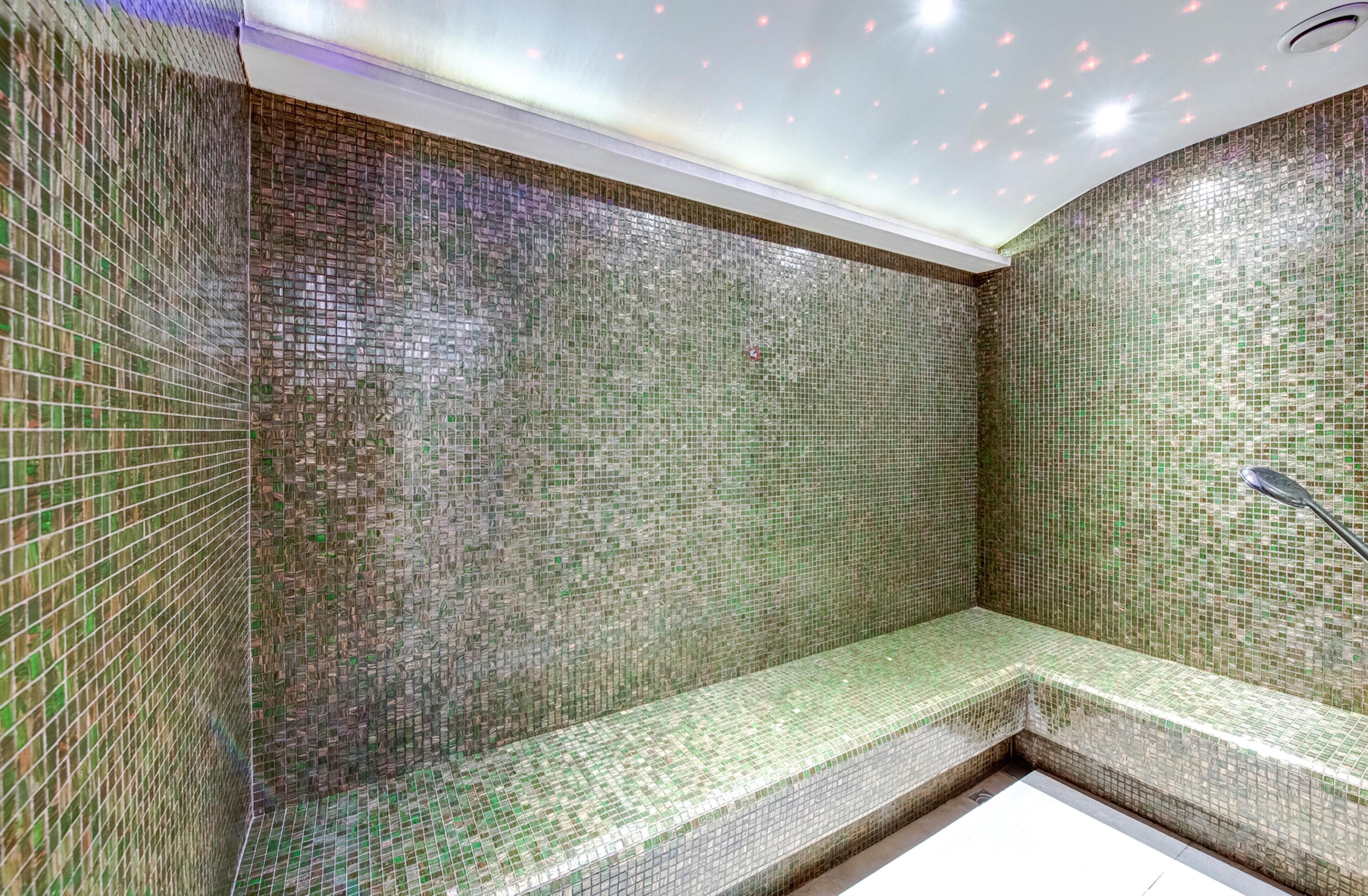 A tiled shower area with a bench, a showerhead, and a ceiling with recessed lighting.