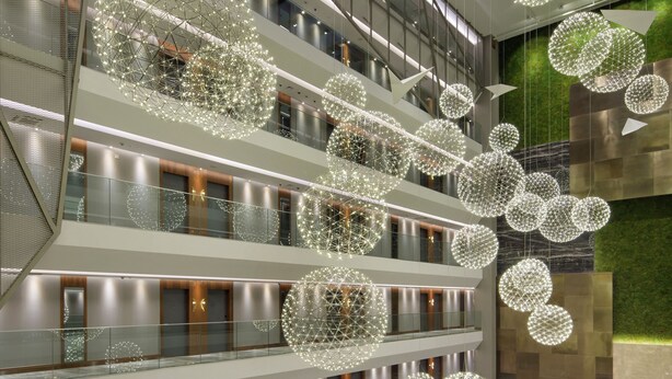 Rebedor d'hotel de diversos nivells amb una zona d'estar àmplia, múltiples plantes i lluminàries esfèriques decoratives.