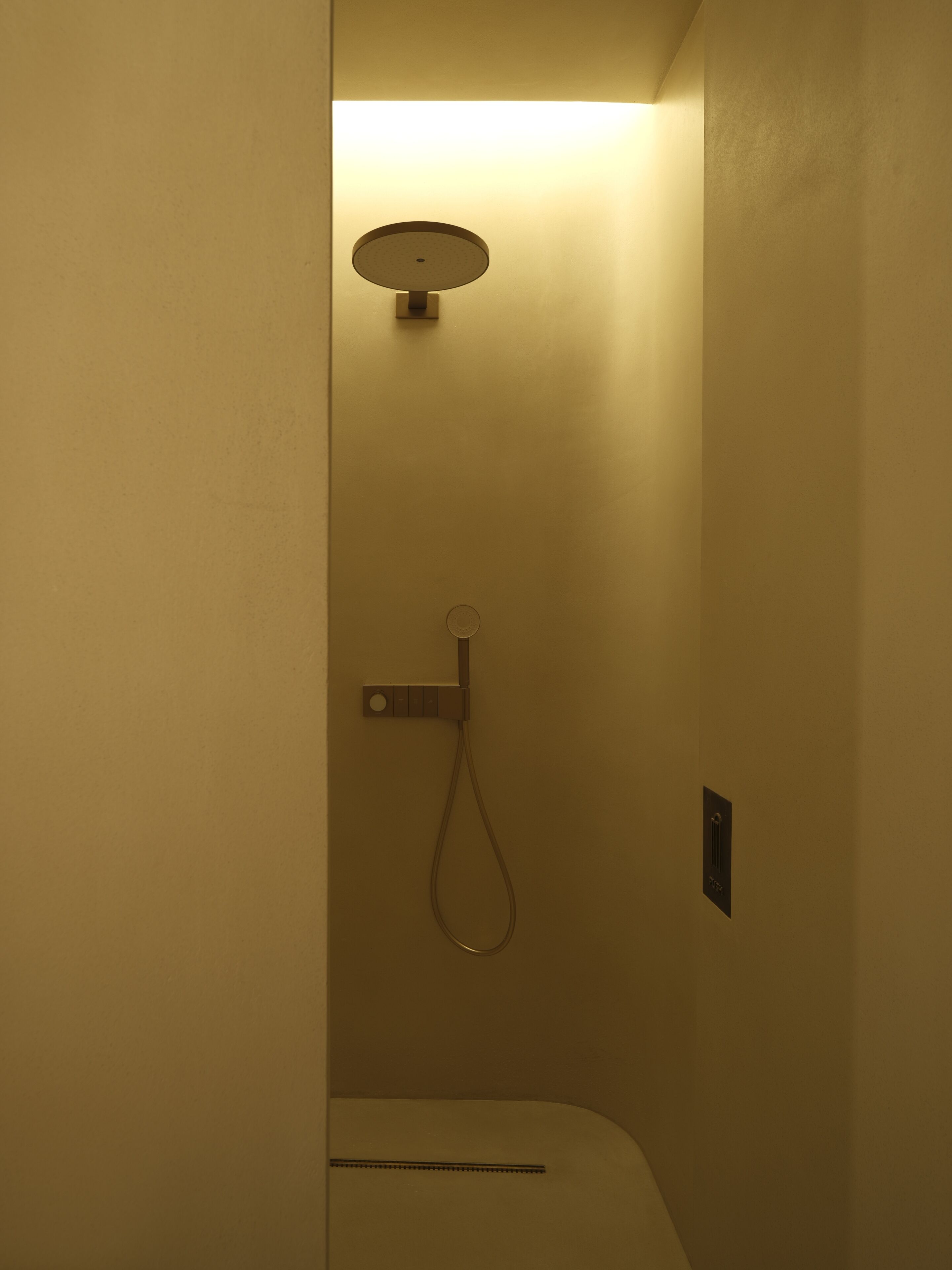 A small, enclosed shower area with a handheld showerhead and a wall-mounted control panel.