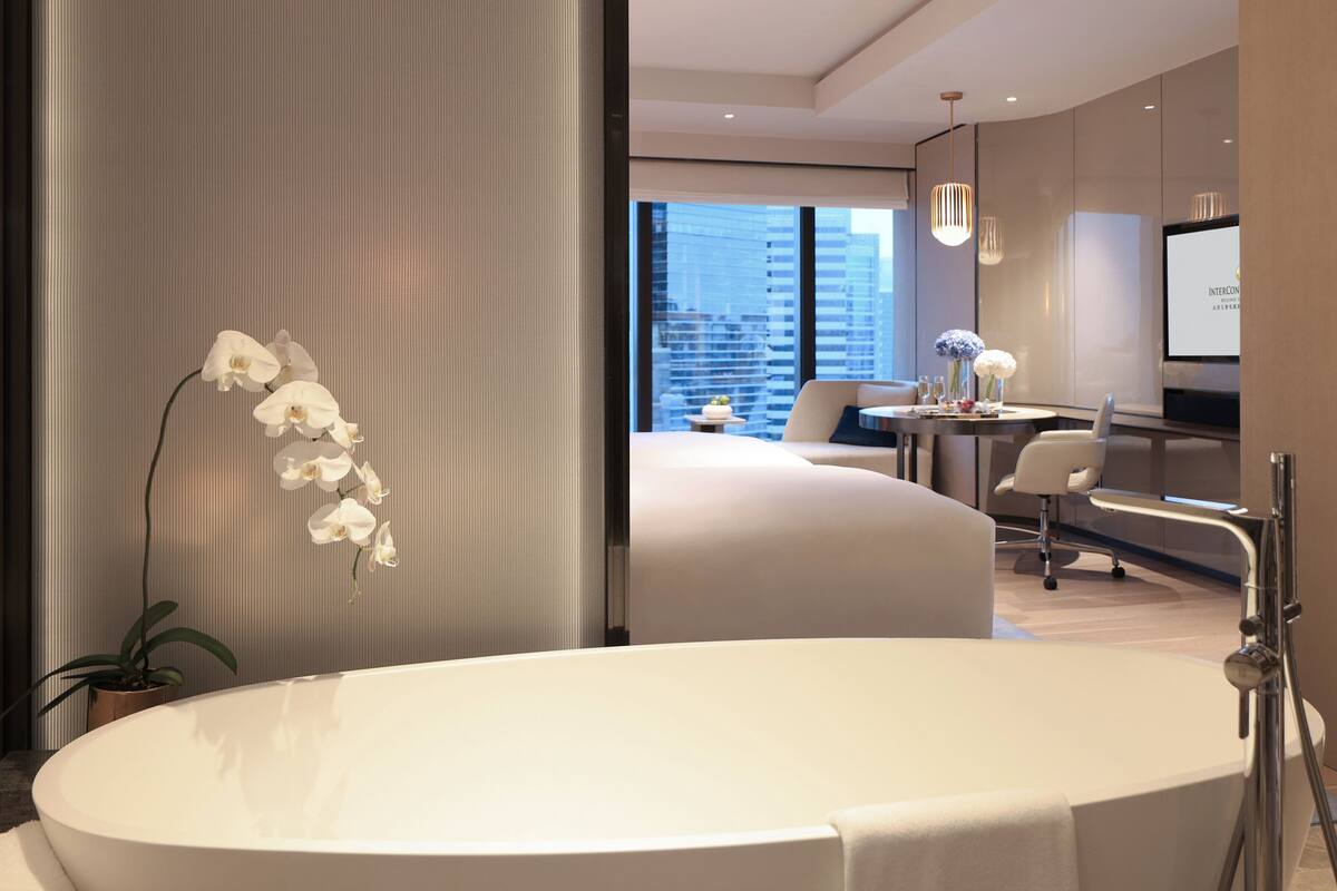 A modern bathroom with a large bathtub, a potted orchid, and a view of the city through large windows.