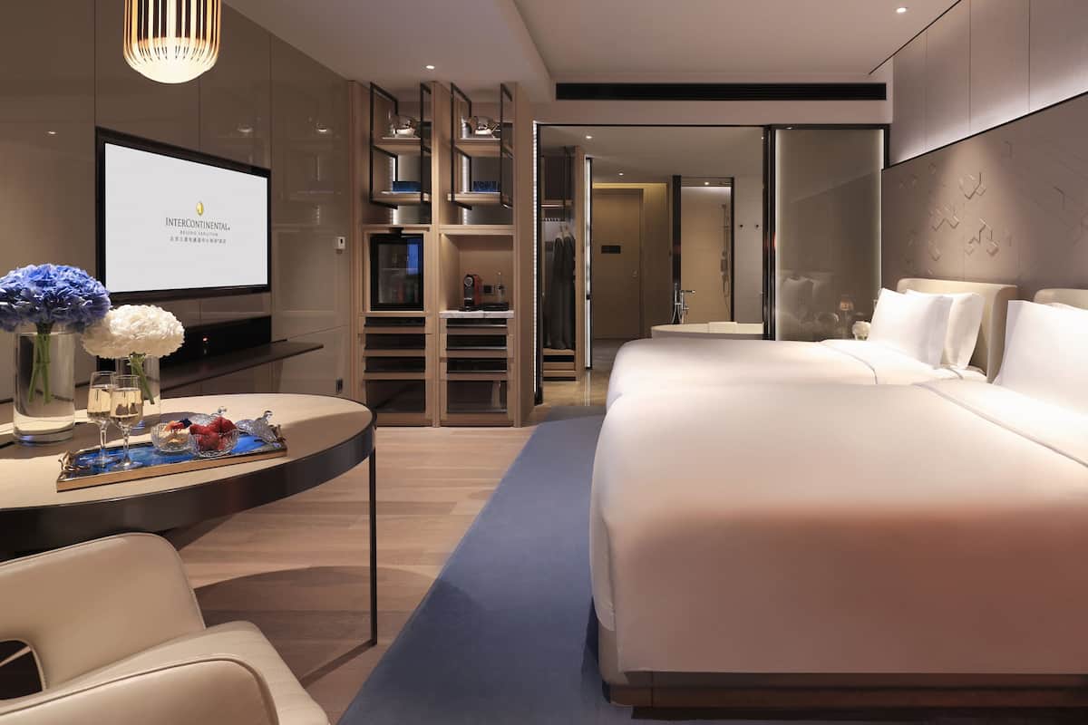 A modern hotel room with a large bed, a desk with a laptop, and a television.